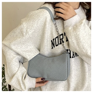 Grey-blue denim crescent bag with silver chain worn by a model in a close-up side view