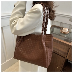 Détail d'un sac cabas marron avec gaufrage pied-de-poule et poignées tressées porté à l'épaule