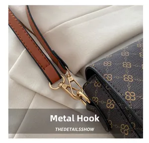 Close-up of golden hardware hook and caramel leather strap on brown monogram shoulder bag