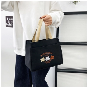 Detail of embroidered naughty bear pattern on a black canvas tote bag with beige handles
