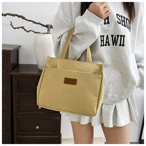Detail view of mustard yellow canvas tote bag with brown leather Sport patch and front pocket
