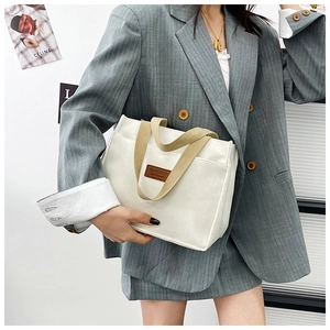 Close-up of the beige canvas tote bag featuring brown leather patch and khaki handles