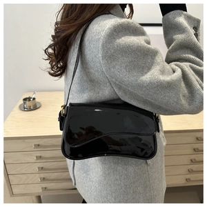 Detail of black patent leather shoulder bag with gold metal buckle and wave edge design