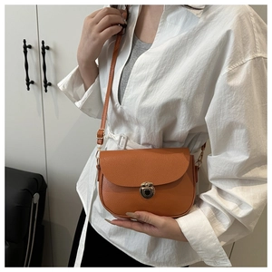 Orange lychee grain leather saddle bag with metal clasp worn by a model in white