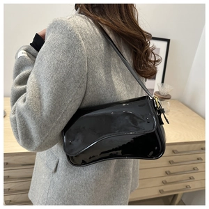 Chic black patent leather underarm bag with asymmetric saddle flap shown on a model