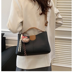 Détail du sac seau en cuir grainé noir avec poignée marron et pendentif dessin animé