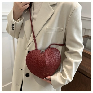 Detail of a red heart-shaped woven crossbody bag with metal zippers on a beige blazer