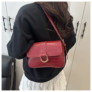 Détail du sac à main rouge texture croco avec boucle en U dorée porté par un mannequin