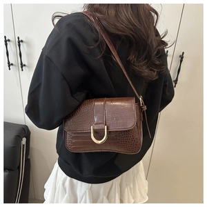 Détail d'un sac baguette marron motif crocodile avec boucle en D dorée sur un mannequin