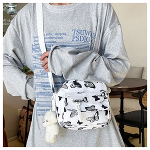 Detailed shot of white nylon crossbody bag with black butterfly patterns and plush bear charm