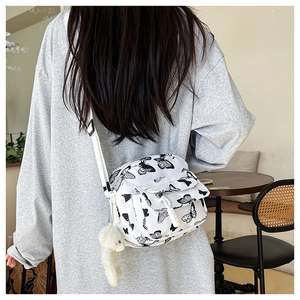 Detail of checkered nylon crossbody bag featuring black butterfly prints and a plush bear charm