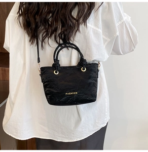 Detail of black pleated bucket bag featuring gold FASHION text and circular handle