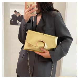 Detail of a metallic gold envelope clutch bag featuring a sleek circular metal buckle