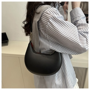 Detail of black crescent hobo bag featuring litchi texture and striking red inner lining