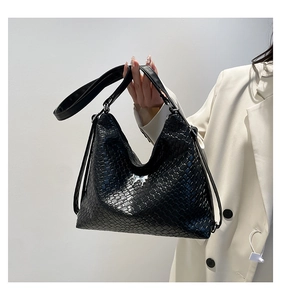 Detail of glossy black woven leather texture and crossbody strap on stylish hobo bag