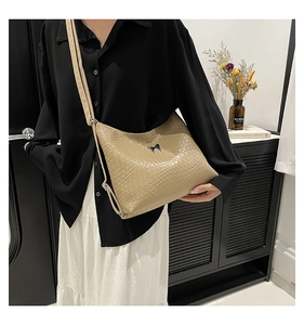 Detail of khaki crocodile embossed shoulder bag featuring a small black bow ornament
