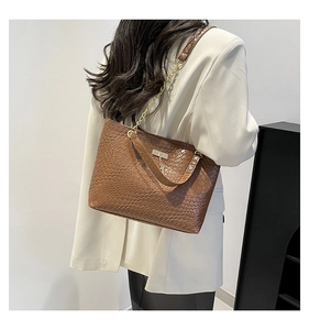 Detail of brown woven tote bag with gold chain strap and square metal plaque shown on shoulder