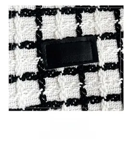Close-up of black and white plaid tweed fabric with FASHION leather patch and gold embroidery