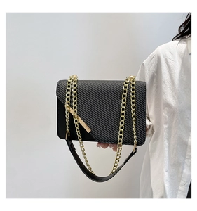 Close-up of black twill crossbody bag with gold chain strap and metal trim details