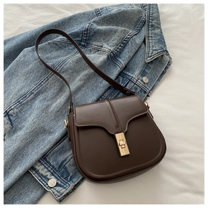 Detail of dark brown matte saddle bag with vintage golden twist-lock on denim jacket