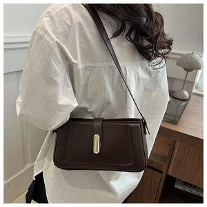 Detailed side view of dark brown leather underarm bag with gold oval clasp on white shirt