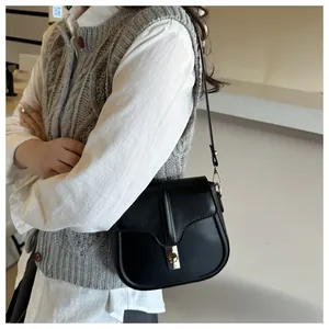 Detail of black matte saddle bag featuring a refined golden clasp and adjustable strap
