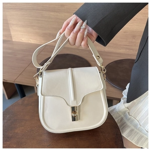 Detailed shot of a creamy white saddle bag with premium leather texture and gold metal lock