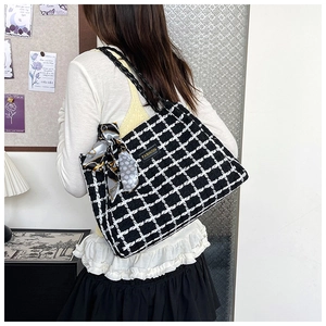 Detail of tweed checkered tote bag with woven handles and decorative scarf accessory