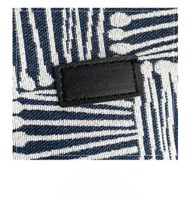 Detail of blue and white woven fabric with a black leather patch and golden logo