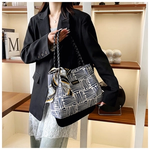 Detail of striped tote bag featuring woven chain handles and decorative silk scarf accessory