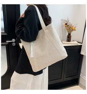 Detail of cream woven tote bag featuring fine mesh texture and white tassel charm
