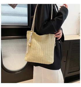 Detail of a beige woven straw tote bag with striped scarf and gold bead charm on a model