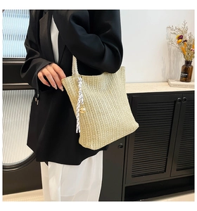 Detail of hand-woven straw tote bag with white tassel and bell charm on model