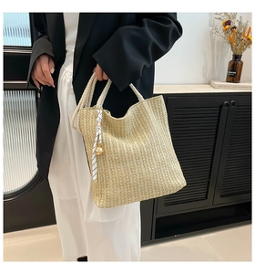 Détail d'un sac cabas en paille tissée beige avec poignées en corde et ruban rayé décoratif