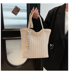 Detail of cream straw tote bag with woven texture, ribbon decor, and golden bell charm