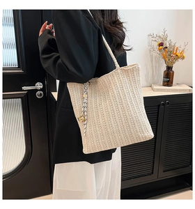 Detail of a beige woven tote bag with a contrasting rope pendant and gold sphere charm