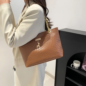 Sac fourre-tout marron tressé avec chaîne dorée et pendentif cerf sur blazer blanc