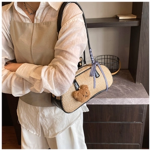 Detail of a straw shoulder bag with black leather trim, plaid bow and teddy bear charm