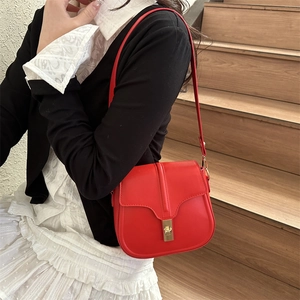 Stylish red leather saddle bag with gold turn-lock closure worn by a model on stairs