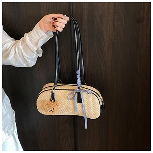 Detail of woven straw bag featuring black shoulder straps, plaid ribbon and teddy charm