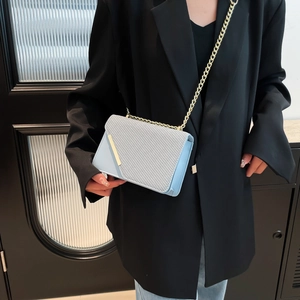 Minimalist light blue square bag with woven texture and gold chain on a black blazer