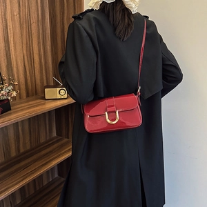 Red patent leather crossbody bag with gold buckle worn over a black trench coat