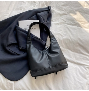 Close-up of black PU leather shoulder bag with vertical stitching and bottom studs