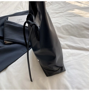 Detail of minimalist black leather tote bag with metal logo on white bedding