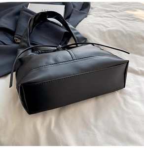 Detail of minimalist black faux leather tote with drawstring design and contrast stitching