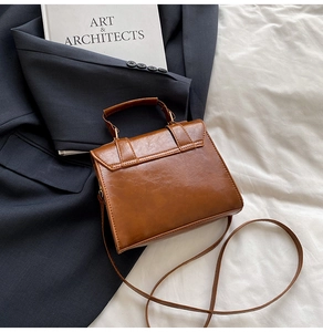 Close-up of a vintage brown leather messenger bag with metal buckle on a blue blazer