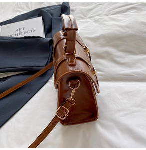 Close-up of brown leather messenger bag side with gold hardware and strap details