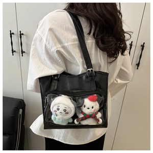 Detail of black PU tote bag featuring a transparent PVC pocket with two plush dolls