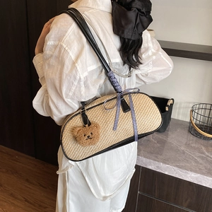 Straw shoulder bag with woven texture, black handles, ribbon bow, and bear charm