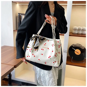 Detail of white corduroy cherry print tote bag with woven handles and floral scarf